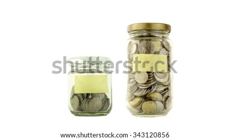 Coins in small and big glass container with blank label white background. Saving money concept. Selective focus and shallow Depth of Field.