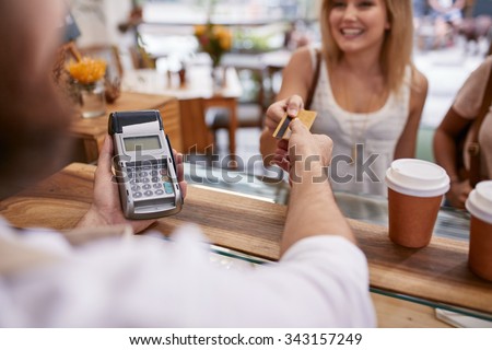 Customer paying for their order with a credit card in a cafe. Bartender holding a credit card reader machine and returning the debit card to female customer after payments.