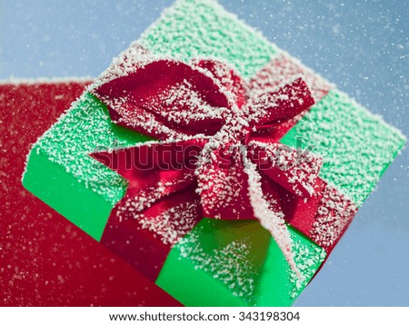 Red Christmas gift box with its lid propped at an angle in front to display the beautiful red ribbon with falling winter snowflakes and copyspace for your greeting or wishes