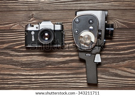 Retro SLR camera and mechanical movie camera on old wooden background