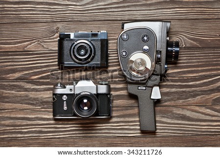 Retro SLR camera, rangefinder and mechanical movie camera on old wooden background