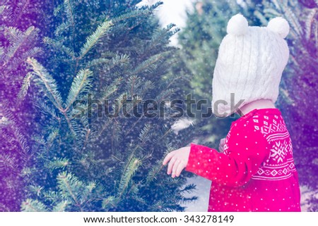 Cute baby girl in red Scandinavian dress at the Christmas tree farm.