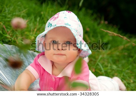 The little girl in a hat is on a grass in park in the summer