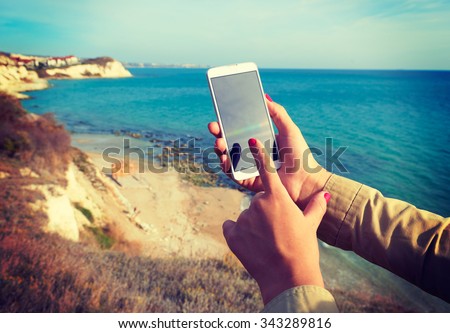 White smart phone on the background Black Sea in female hands, instagram effect