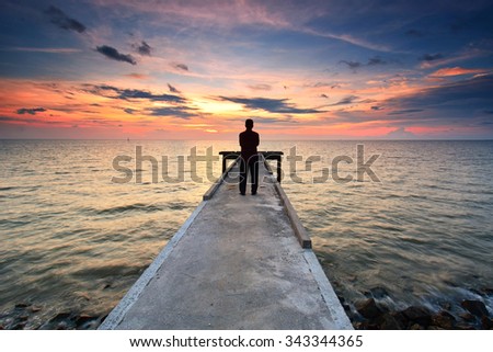 A silhouette man standing on jetty towards the sea horizon during sunset. Nature composition.