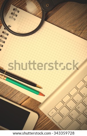 notebook on a spring, pencil, pen, smart phone, computer keyboard and magnifying glass on the surface of an old wooden table. mockup. instagram image filter retro style