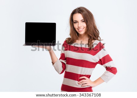 Portrait of a casual smiling woman showing blank laptop computer screen isolated on a white background