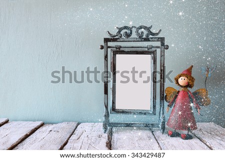 low key image of old victorian steel blue blank frame and cute fairy on wooden table. glitter overlay 
