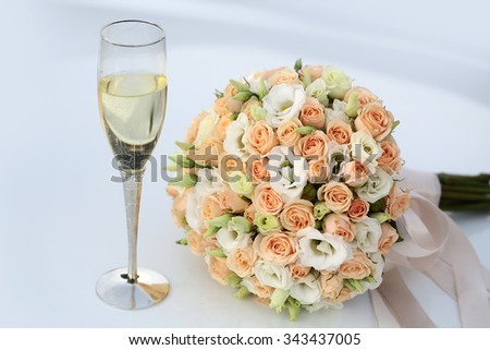Photo front view side-on ball-shaped elegant wedding bouquet of fresh pastel pink white roses flowers with ribbons for bridal ceremony champagne glass on white indoor background, horizontal picture
