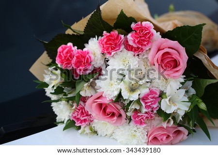 Photo closeup front view elegant colorful bouquet of fresh pink white roses chrysanthemum flowers green leaves in plain florist paper packaging on grey indoor background, horizontal picture 