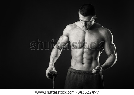 The athlete pours beer from a bottle on the floor. Disregard athlete to bad habits. Black and white photo Muscular man on a dark background. Photos for sporting and social magazines and websites.
