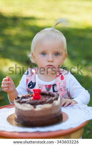 Happy child is outside in the park. She is looking at camera and celebrating the first year of  her birthday with cake.