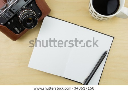 Old camera, notebook, pen and a cup of coffee on wooden surface