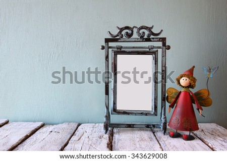low key image of old victorian steel blue blank frame and cute fairy on wooden table