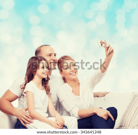 family, holidays, technology and people concept - smiling mother, father and little girl making selfie with camera over blue lights background