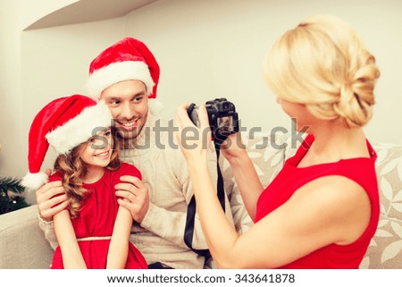 family, christmas, x-mas, happiness and people concept - mother taking picture of smiling father and daughter in santa helper hats