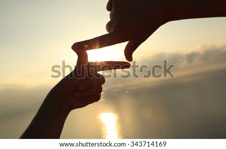 frame making of hands against bright sea sunrise and sunny golden way at water