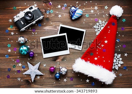 Christmas and New Year background with old fashioned camera, red Santa's hat, photo frames and christmas decorations - stars, silver snowflakes, confetti on wooden table. Place for your text. Mock up.