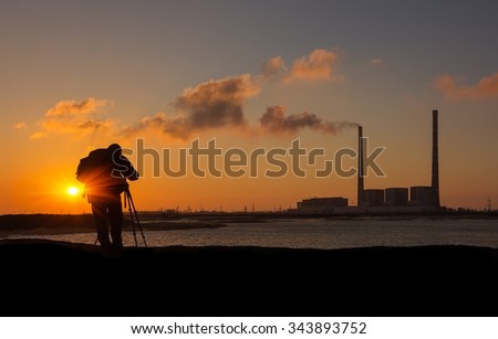 photographer at sunrise on the coast, on a background of giant pipes power