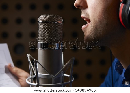 Man Holding Notes And Talking Into Studio Microphone Royalty-Free Stock Photo #343894985