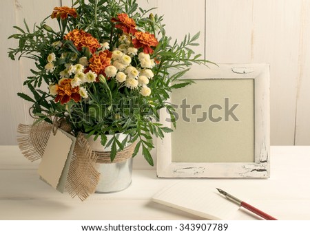 Retro photo frame and old pen with sheet paper and tagetes bouquet on wooden board in shabby chic style