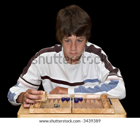 A young teenage boy playing a game of backgammon. The boy and board are isolated over a black background.