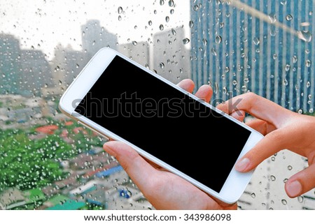 woman hand hold and touch screen smart phone, tablet,cellphone on abstract blurred rain drop on glass in city background.