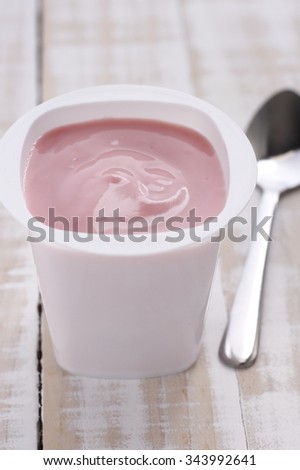 strawberry yogurt in white plastic cup with spoon on wooden white background.  