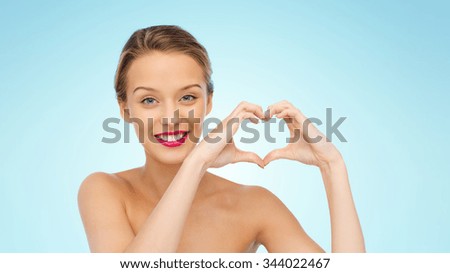 beauty, people, love, valentines day and make up concept - smiling young woman with pink lipstick on lips showing heart shape hand sign over blue background