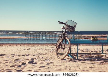 Retro styled  photo of bicycle near bench on beach.