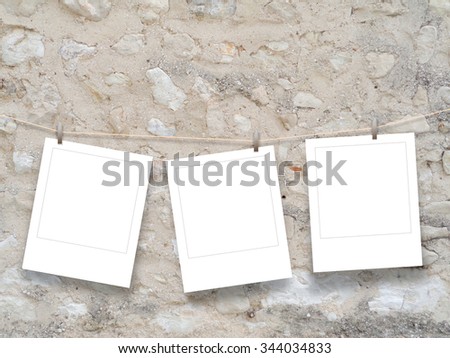Three blank instant photo frames hung by clothes pin on brown old stone wall background