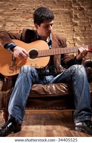 Young man playing on guitar sitting in a chair.
