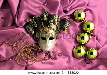 Background of golden Christmas tree balls with gold decorations and golden mask on soft pink shiny silk fabric with dramatic light and shadow