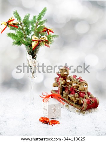 Christmas tree in white decorative goblet, white gift box, red and gold toy bears on sledge, candies and snow on retro vintage white table on white blurred background