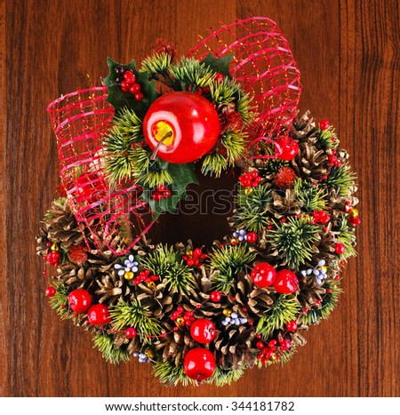Christmas wreath with red and gold bauble decorations, bow, holly, mistletoe, pine cones and blue  on wooden background, place for text