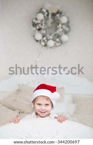 The little girl playing in the bedroom on the big bed in the caps of Santa Claus, Christmas Eve, New Year