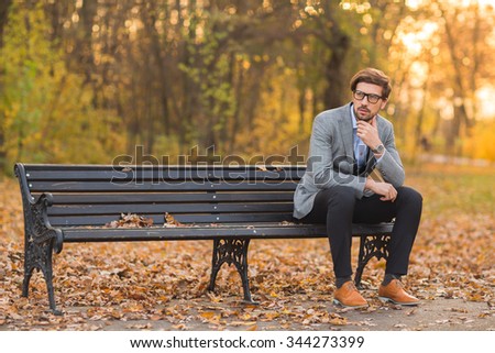 Autumn fashion style man in the park on the bench Royalty-Free Stock Photo #344273399