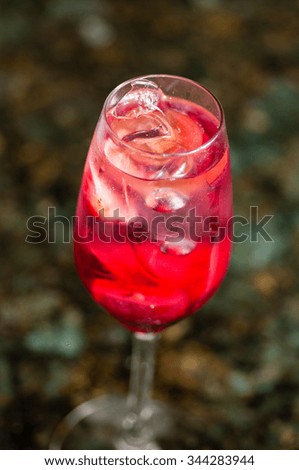 close-up of one misty champagne flute filled with red liquid and ice cubes, on a blurry earth and leaves background