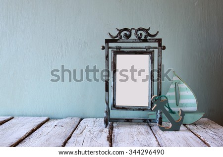 low key image of old victorian steel blue blank frame and wooden sailing boat on wooden table 