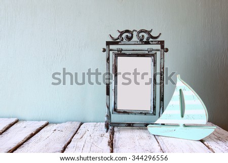 image of old victorian steel blue blank frame and wooden sailing boat on wooden table 
