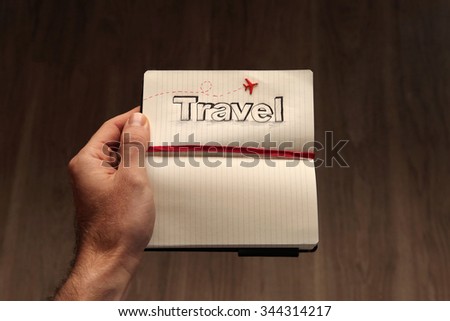 The word travel sketched on a open notebook and held by a male traveler, dreaming about all the foreign destinations he wants to visit across the globe.  