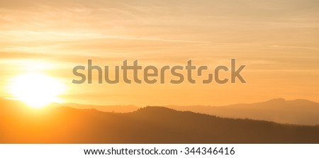 Photo panorama of beautiful surrealistic spectacular orange sunset behind mountain range over cloudy sky with fog on ridge silhouette background, horizontal picture
