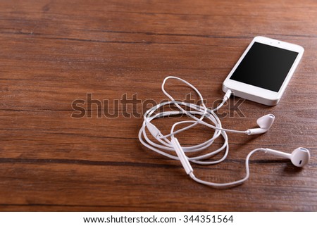White cellphone with headphones on varnished wooden background