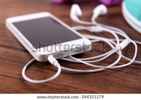 White cellphone with headphones and pink dumb bells and gumshoes on varnished wooden background, close up
