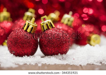 Red Christmas balls on snow against red bokeh background.