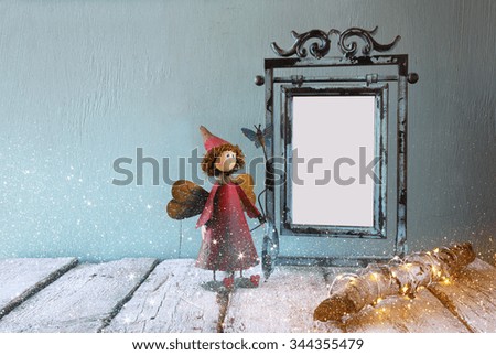 low key image of old victorian steel blue blank frame, tree log with fairy lights and cute fairy on wooden table 