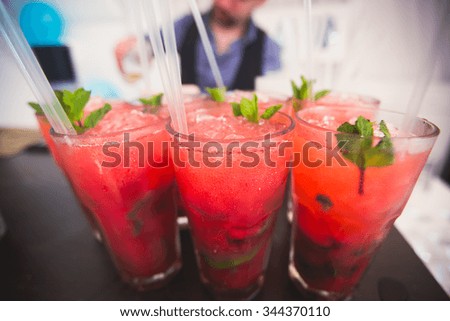 Beautiful row line of different colored alcohol cocktails with mint on a party, martini, vodka with bubbles,and others on decorated catering bouquet table on open air event, picture with bartender