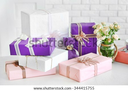 Composition of colourful gift boxes and flowers in glass on white table in front of brick wall background