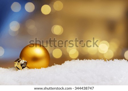 Image of a golden bauble on artificial snow with bokeh lights in background and free space