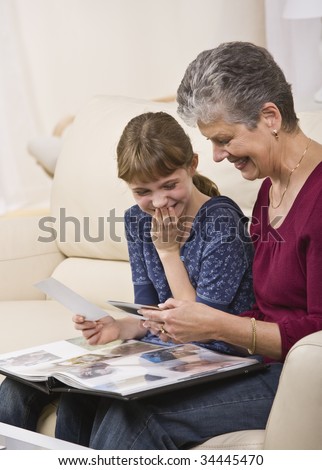A grandmother looking through a photo album with her granddaughter.  They are both smiling.  Vertically framed shot.
